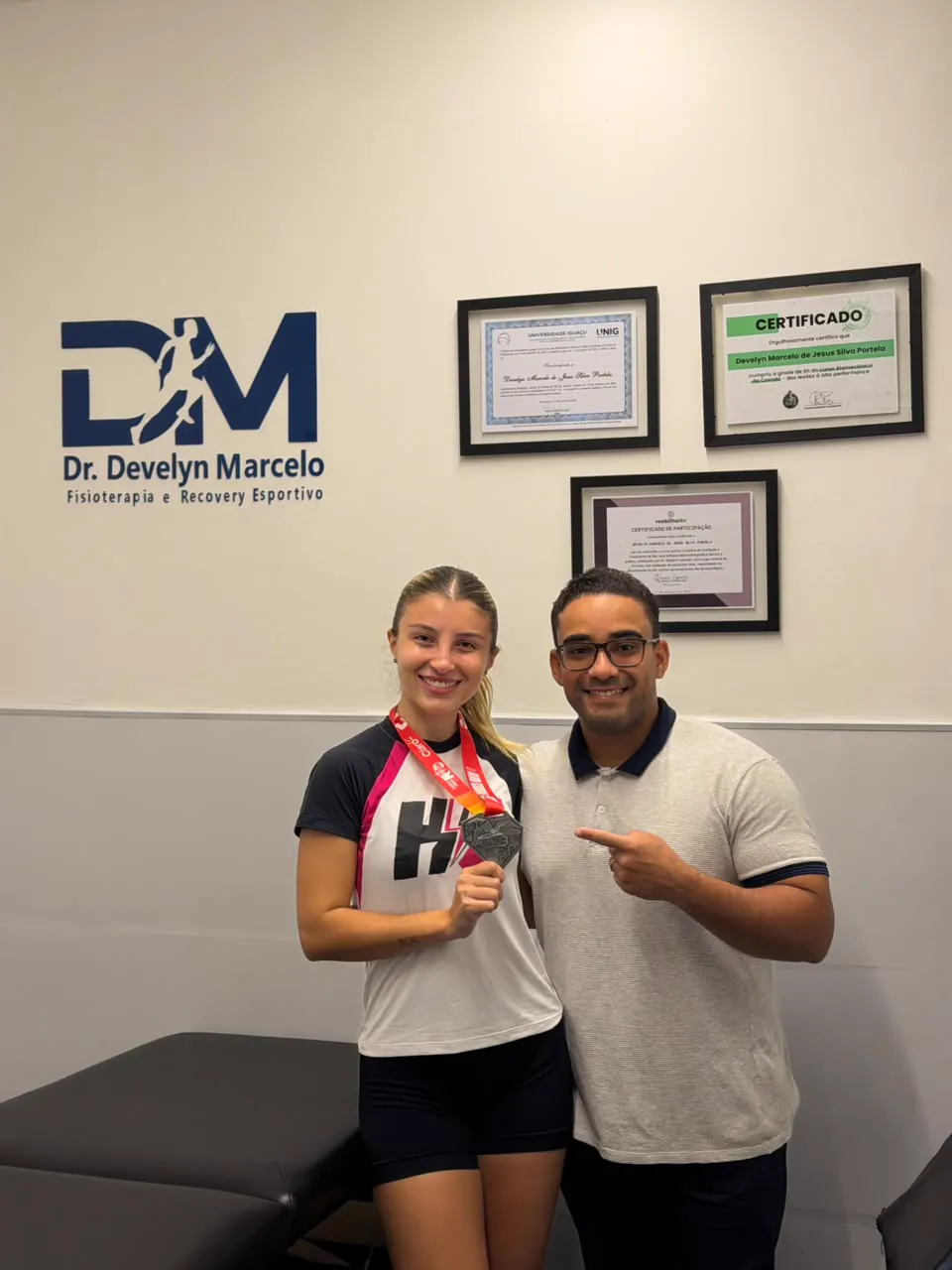 Paciente comemorando medalha de prova ao lado do Dr. Develyn no consultório