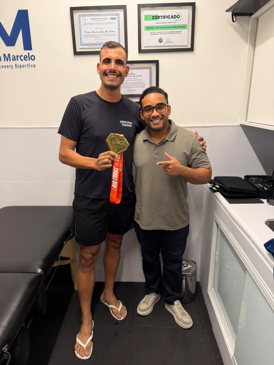 Dr. Develyn e paciente medalhista em frente aos certificados do consultório