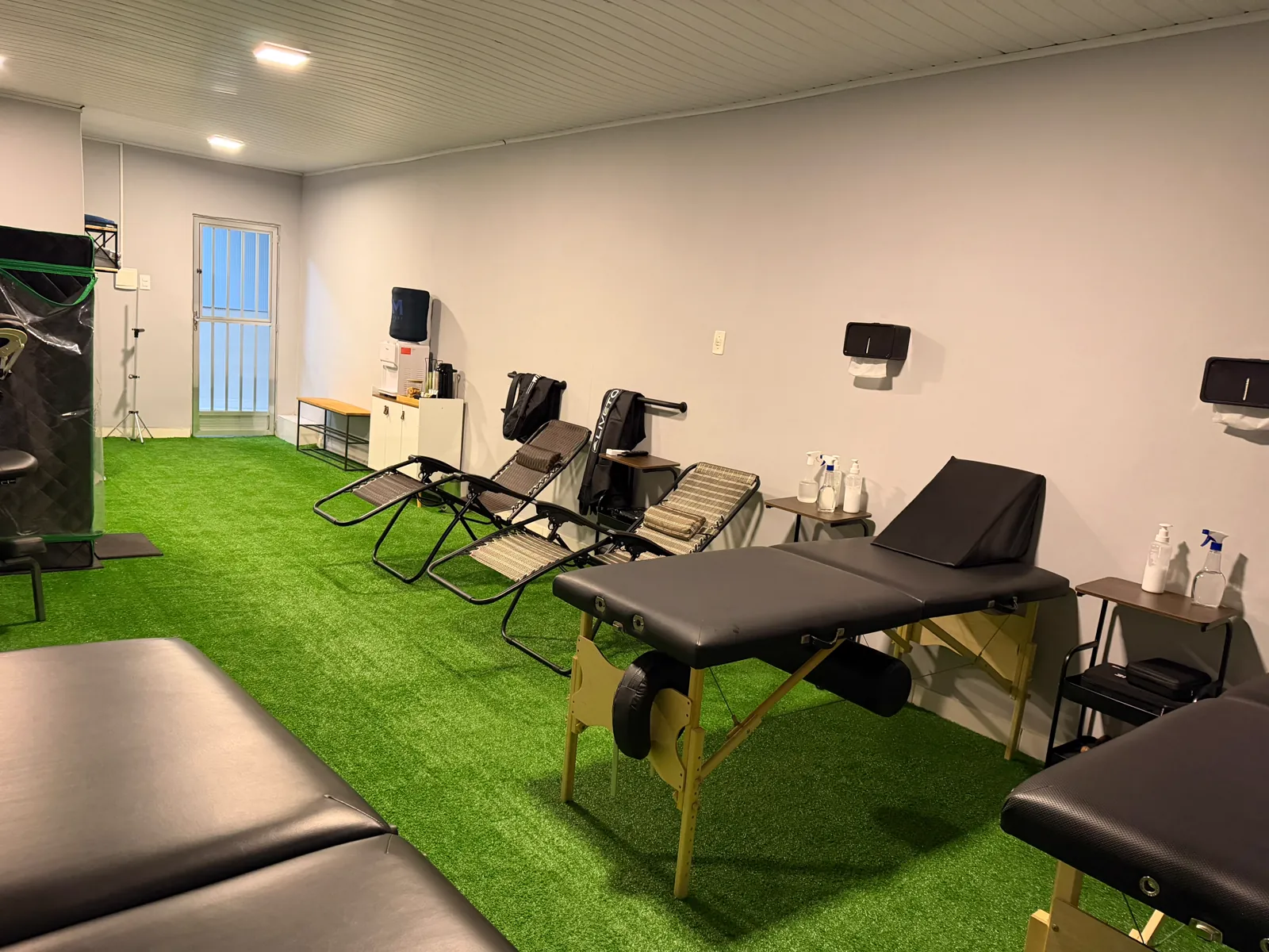 Sala de recovery ampla com macas de atendimento, cadeiras reclináveis zero-gravity e sauna ao fundo